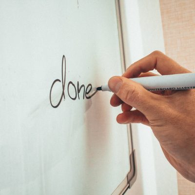 Crop unrecognizable male coach writing done word on whiteboard during presentation in light office